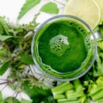 Boisson verte dans un verre, entourée d'herbes fraîches, symbolisant la détoxication du foie.